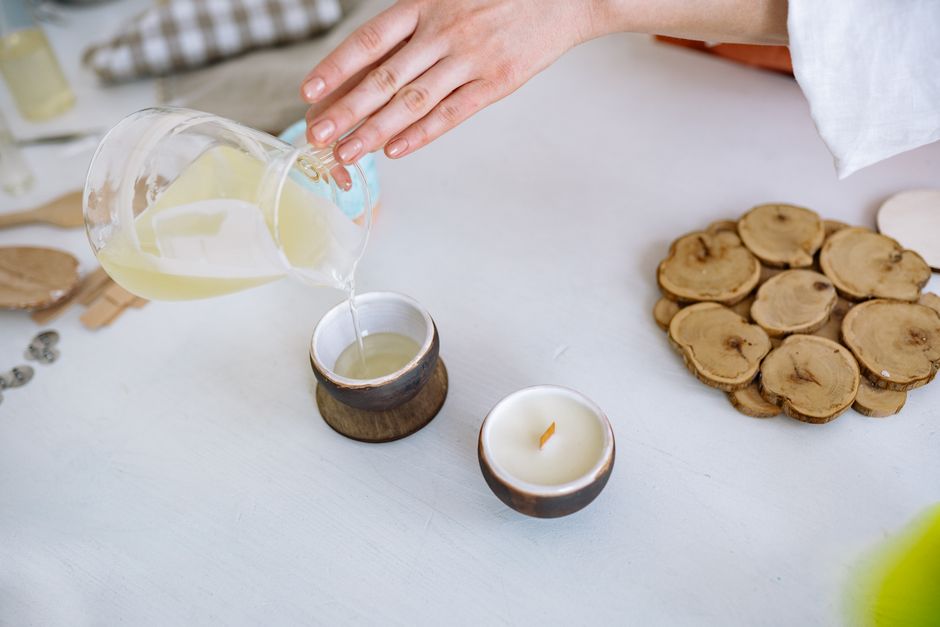 Close-up of hand pouring candle wax into rustic container, crafting essentials nearby.