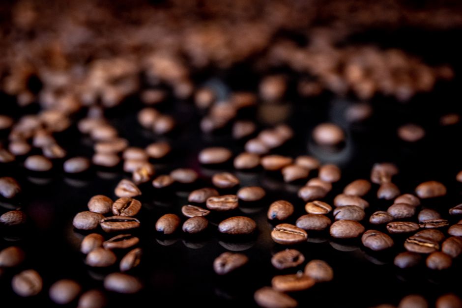 Aromatic coffee beans scattered over a black surface, showcasing rich textures.
