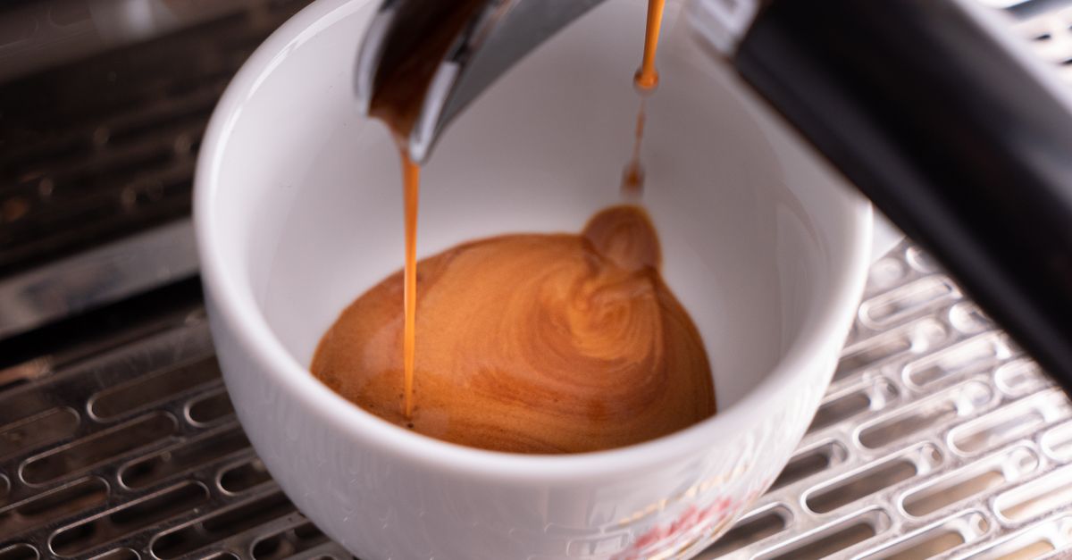 A detailed view of espresso coffee being poured into a white cup from a machine, highlighting the rich crema.