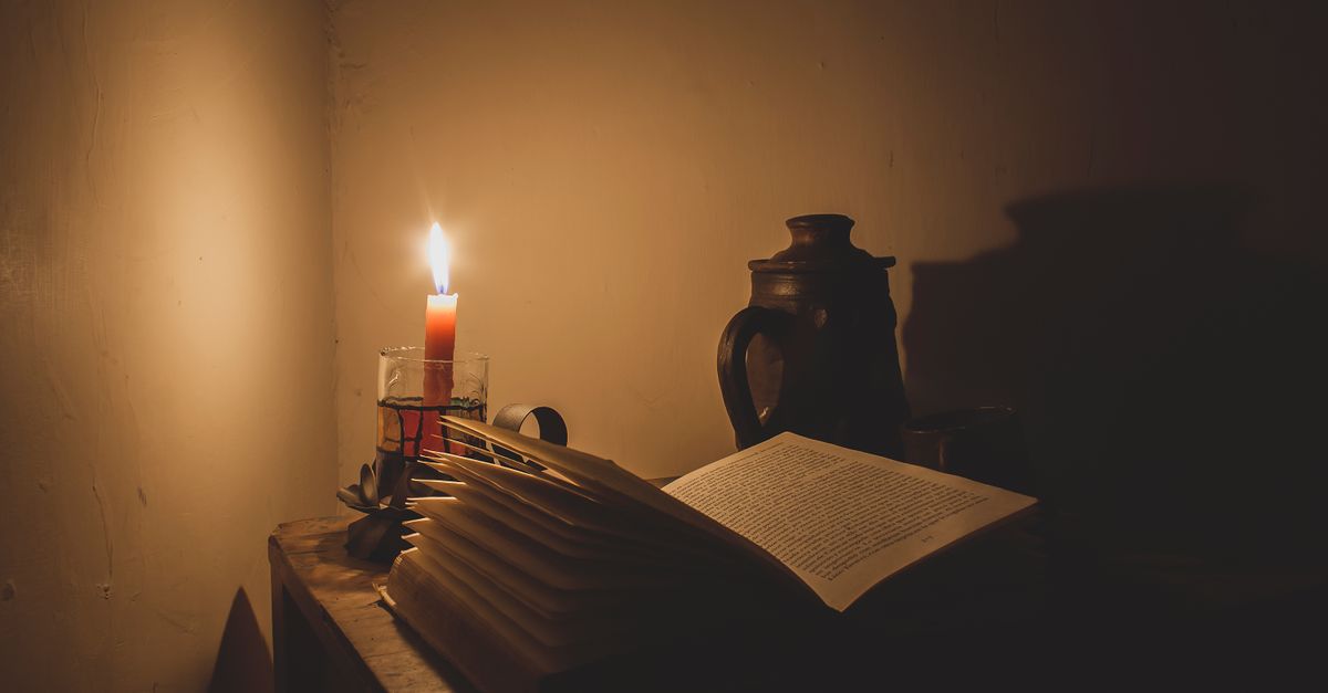 A moody candlelit scene featuring an open book, vase, and subtle shadows enhancing a vintage ambiance.