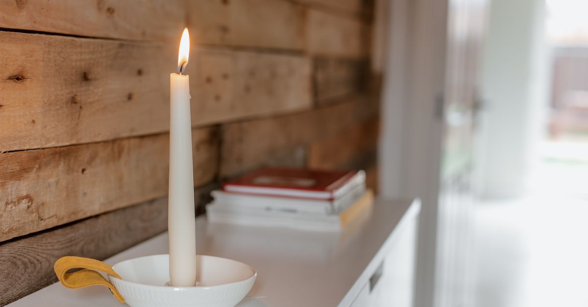 Burning wax candle in bowl near heap of literature on table in light house