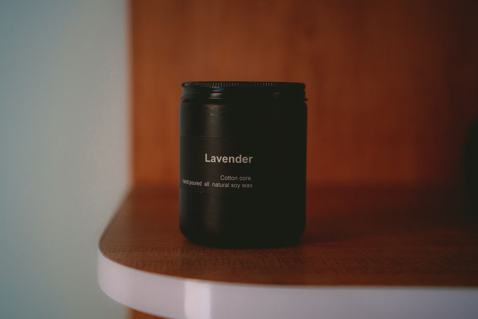 A lavender scented soy wax candle on a wooden shelf in soft light.