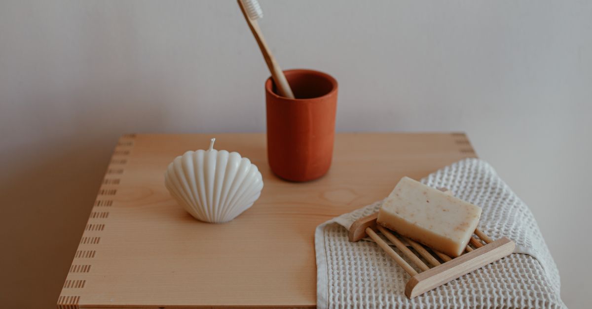 Stylish minimalist bathroom decor showcasing wooden soap dish, candle, and toothbrush on wooden shelf.