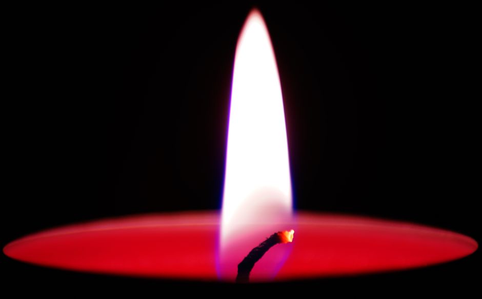 Detailed shot of a red wax candle with a bright flame against a dark background.