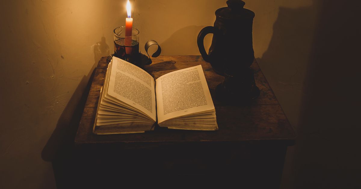 A warm, atmospheric scene of an open book by candlelight on a wooden table with a dark vase, creating a tranquil reading nook.