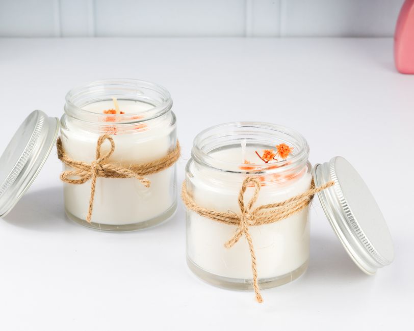 Two rustic candles in jars with orange flowers, tied with twine on a white surface.