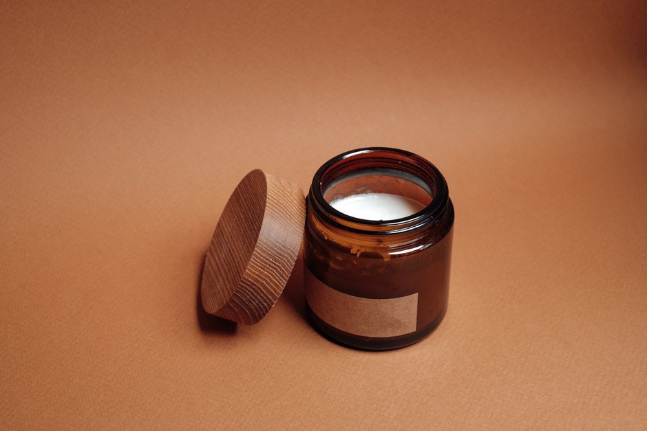 A brown jar with an open lid and candle inside on a brown background, perfect for relaxation themes.