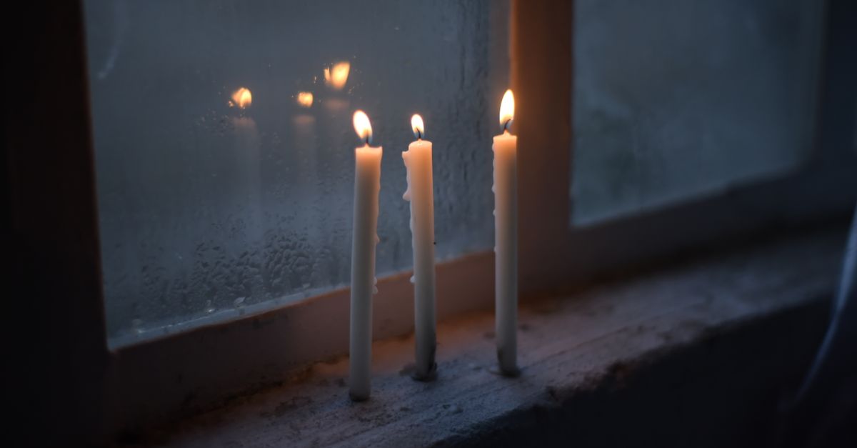Three candles burning on a window sill create a reflective and serene atmosphere.