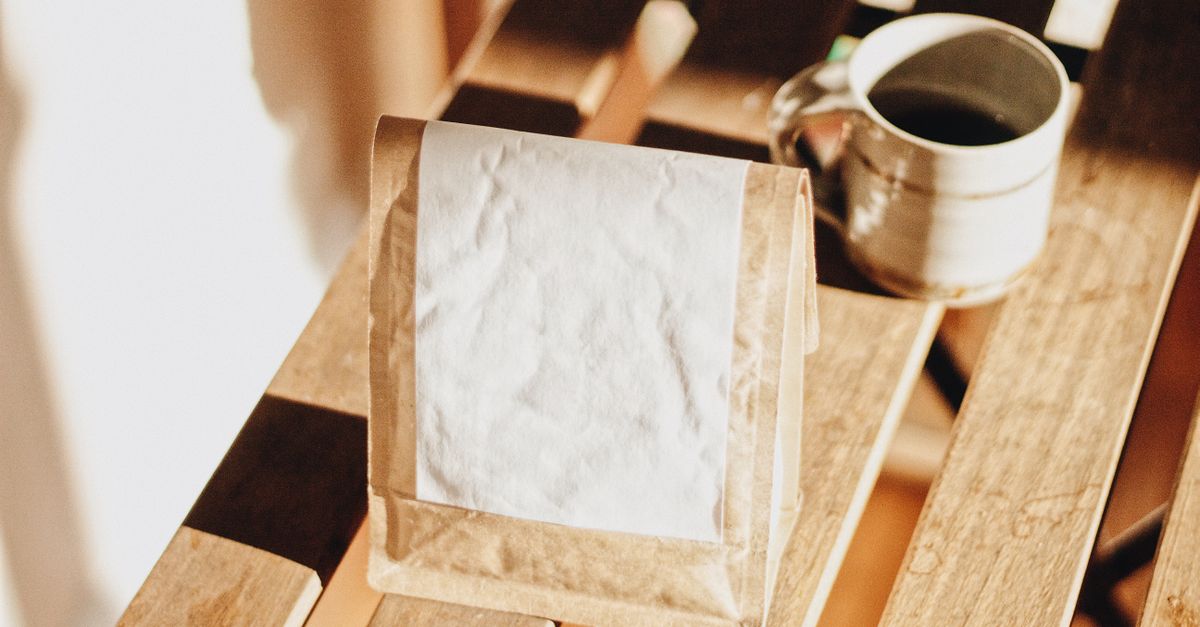 Rustic coffee setup with a ceramic mug and craft paper bag on a wooden table.