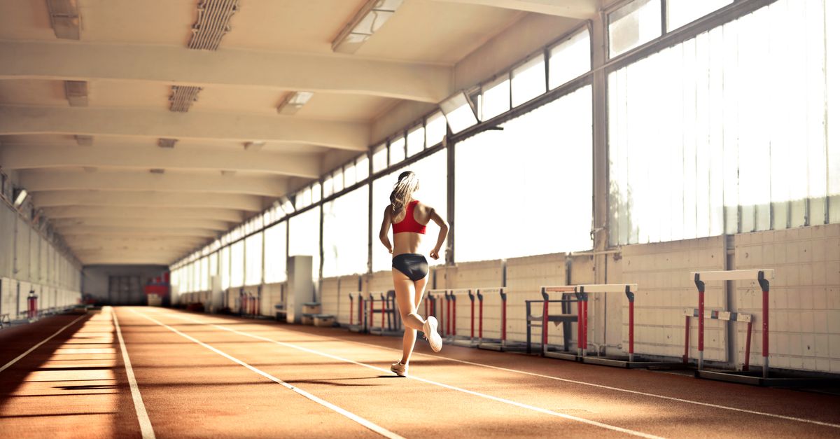 Woman in athletic wear running on an indoor track, showcasing speed and determination.
