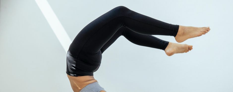Crop anonymous barefoot female in black leggings doing yoga Scorpion pose in light room