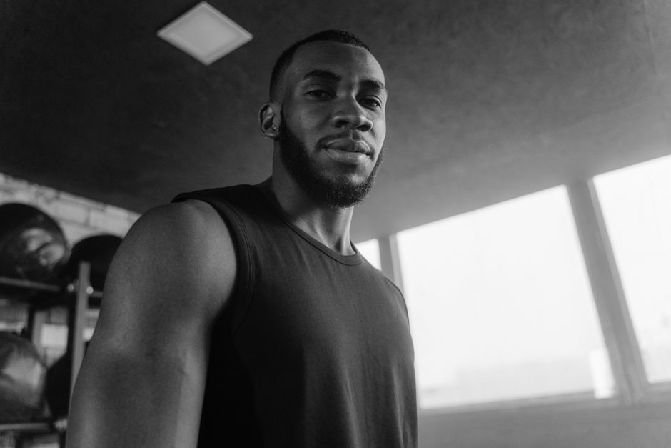Grayscale photo of a strong man in a gym, wearing a tank top, looking confident.