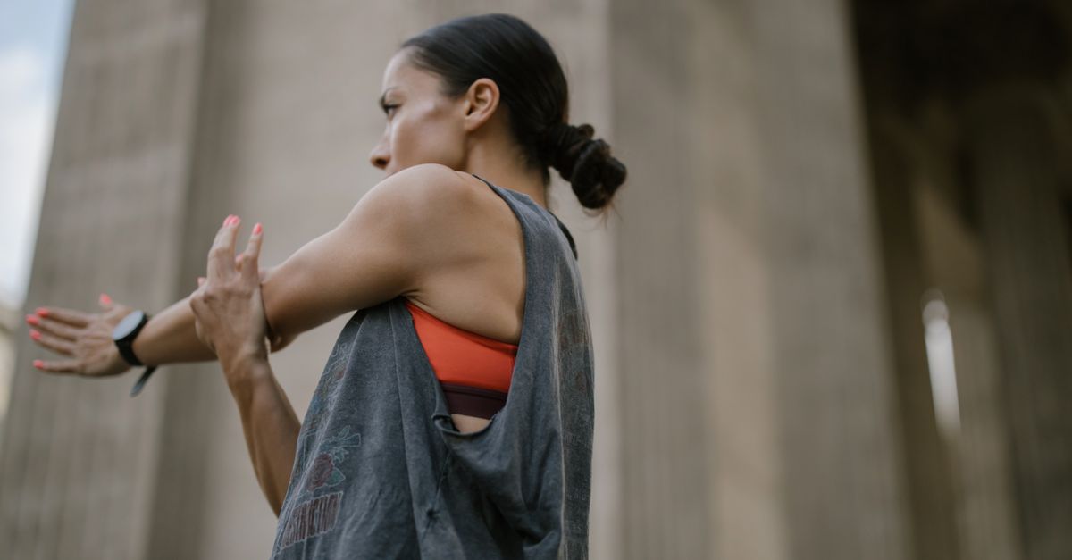 Woman in athletic wear stretching outdoors in a cityscape background.