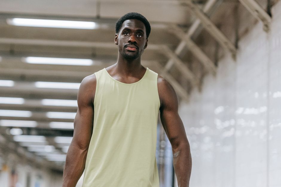 Muscular man in a tank top walking through a modern subway station.