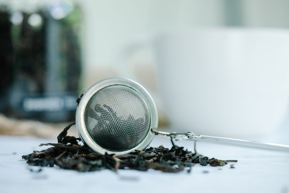 Metal tea infuser surrounded by loose tea leaves in a serene setting.