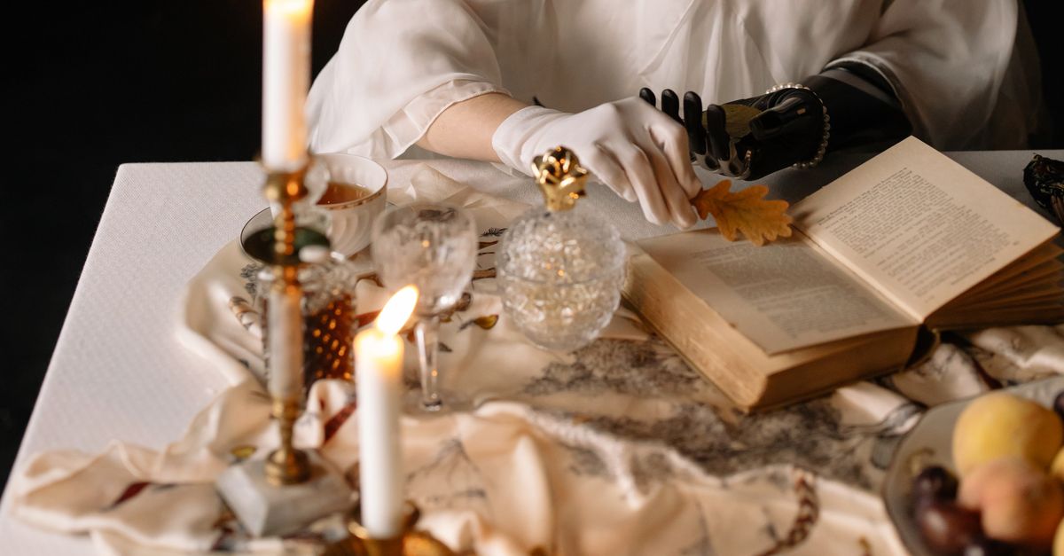 A candlelit table with an open book, brass candle holders, and autumn decor creates a warm, vintage atmosphere.