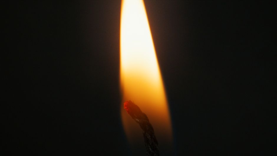 Close-up image of a candle flame against a dark background, illuminating a warm glow.
