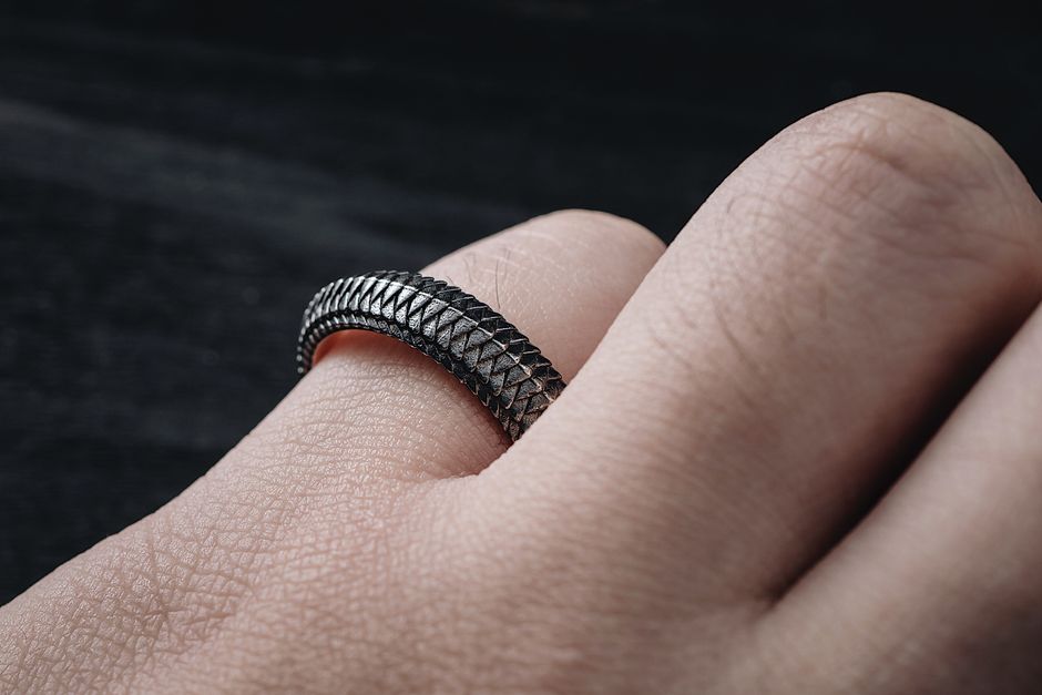 Detailed macro shot of a textured metal ring resembling snake scales worn on a finger.