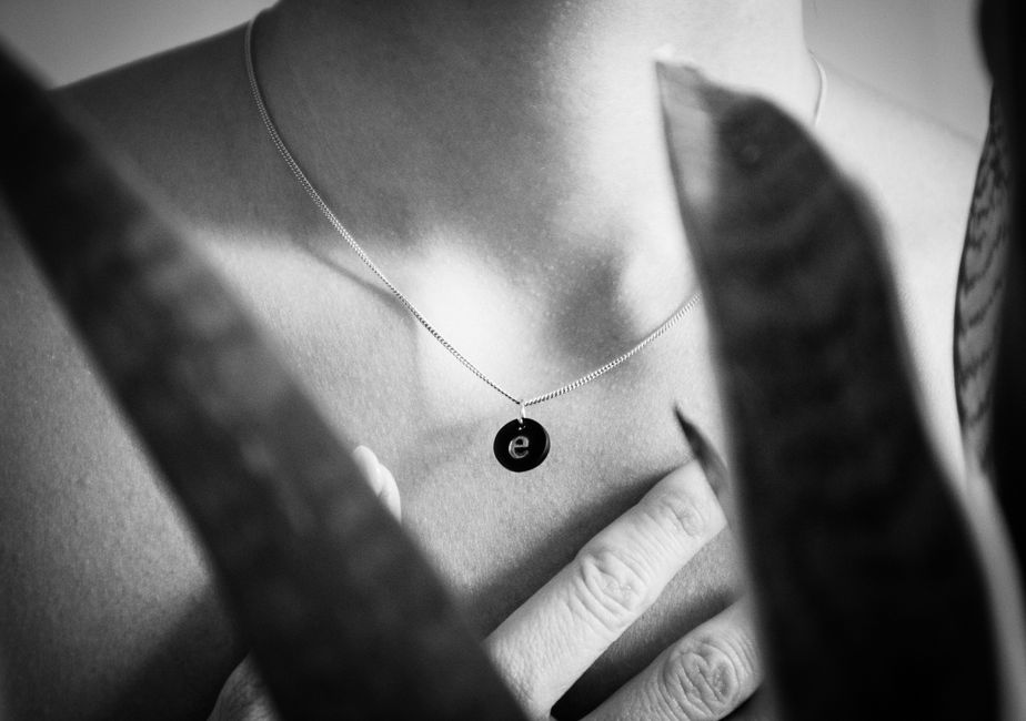 Close-up of a necklace with a pendant on bare skin in black and white.