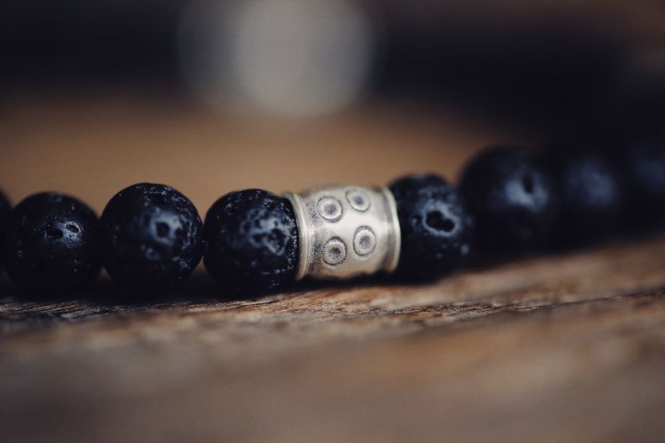 Detailed close-up of a beaded bracelet with dark textured beads and a decorative metal accent piece.