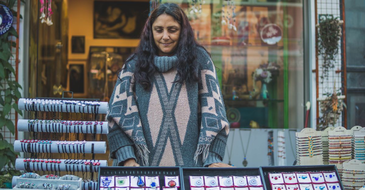 A woman displaying handmade jewelry at a vibrant street market stall.