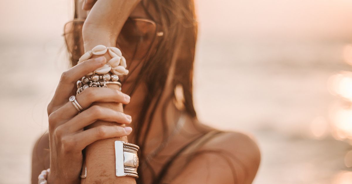 A woman posing with stylish jewelry on a beach during sunset.