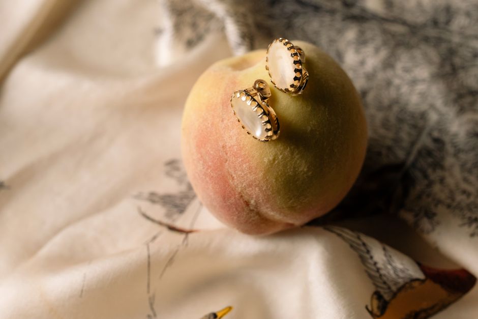 Close-up of elegant earrings on a ripe peach, showcasing jewelry and fresh fruit contrast.