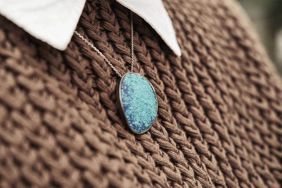 A stylish blue pendant necklace resting on a brown knit sweater for fashion elegance.