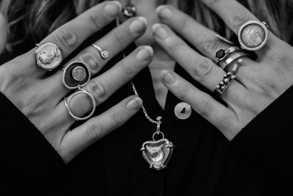 Close-up of hands adorned with various silver rings and necklace, showcasing fashion style.