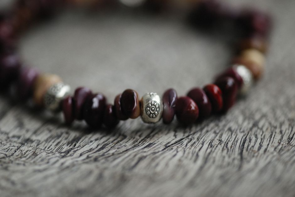 Elegant bracelet with red stones and metal beads on wooden surface.