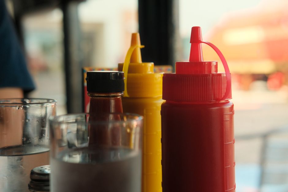 Ketchup, mustard, and sauce bottles on a restaurant table with glasses.