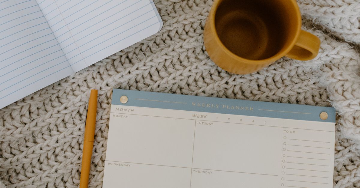 Flat lay of a planner, notebook, and coffee mug on a knitted blanket for a cozy planning session.
