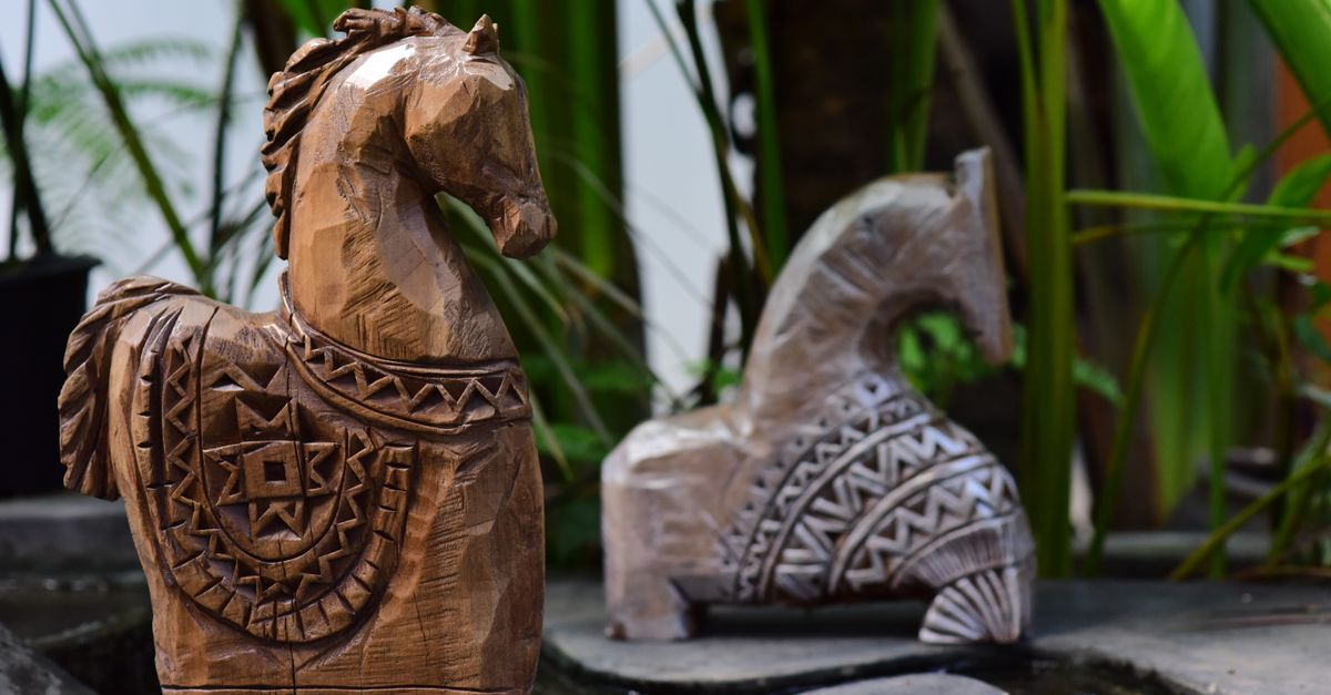 Wooden horse sculptures with detailed carvings displayed outdoors amidst lush greenery.