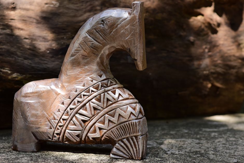 A beautifully carved wooden horse figurine with detailed patterns, set against a natural outdoor background.